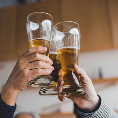 A group of hands clinking three beer glasses in a toast.