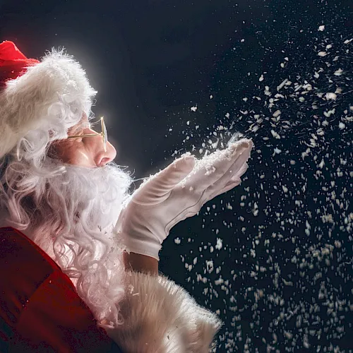 A Santa in red and white tosses glittery flakes/confetti into the night sky.