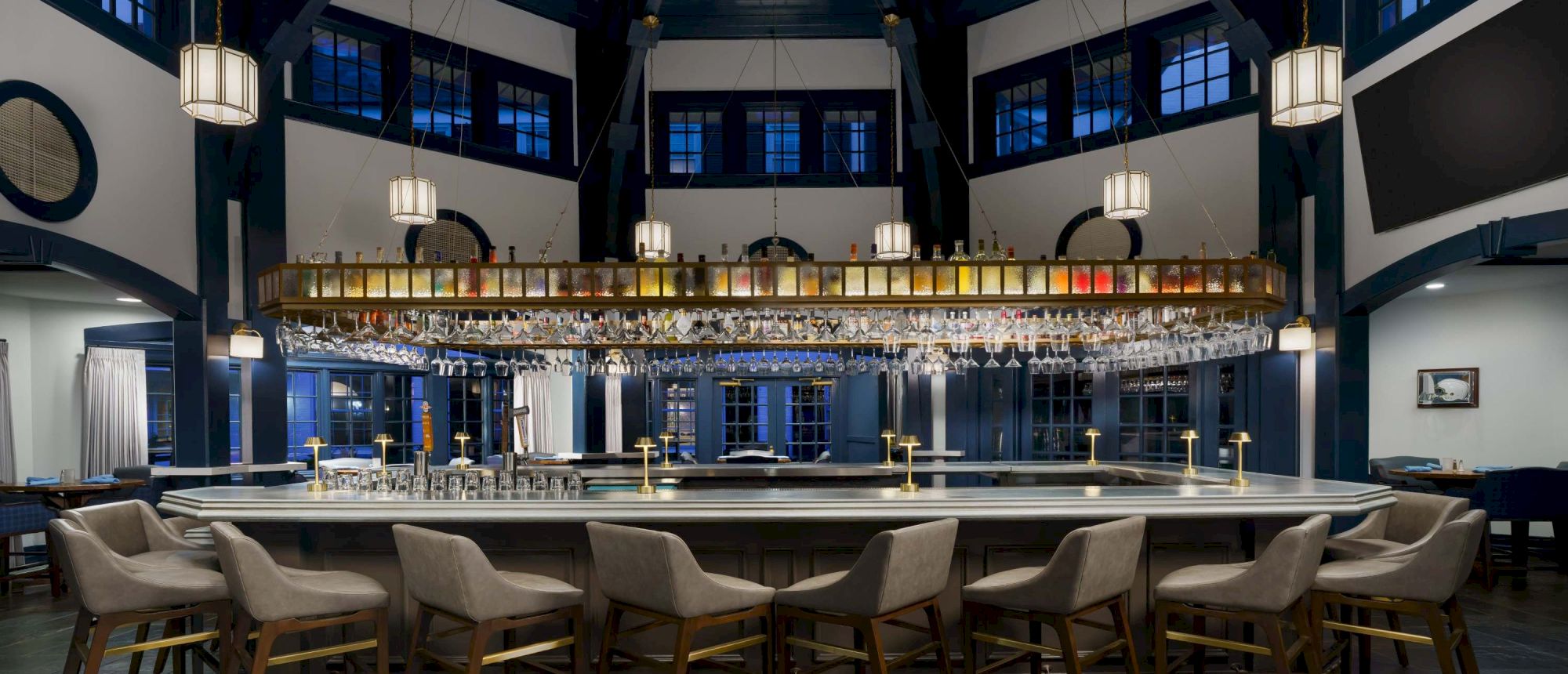 A stylish, dimly lit bar with a long counter, hanging lanterns, and blue-accented walls; modern chairs line the bar in a cozy setting.