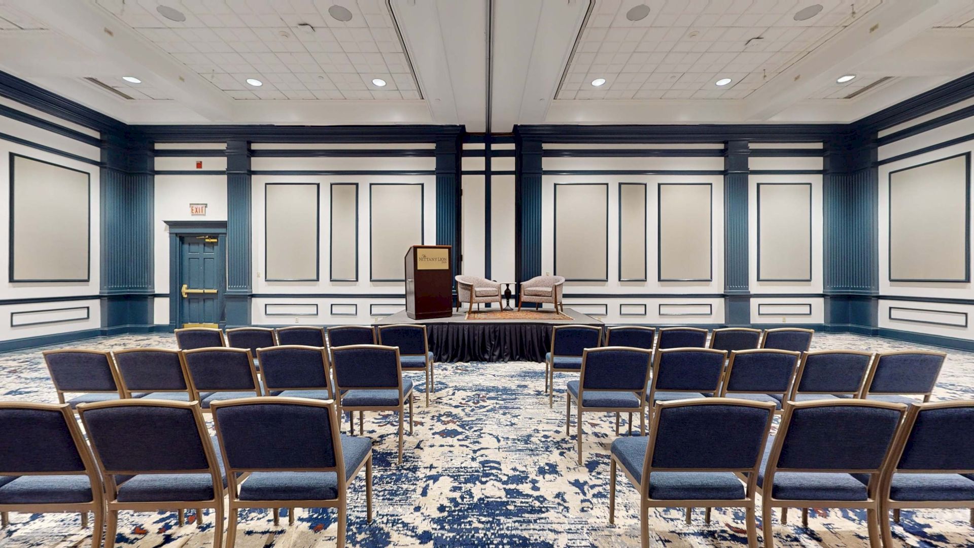 A conference or meeting room set up for a presentation, with chairs facing a stage and podium.