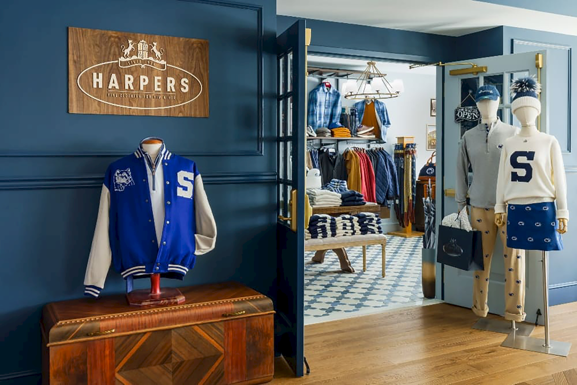 A fashion store display for &ldquo;HARPERS,&rdquo; with mannequins wearing varsity-style and knit outfits, plus folded clothes on shelves.