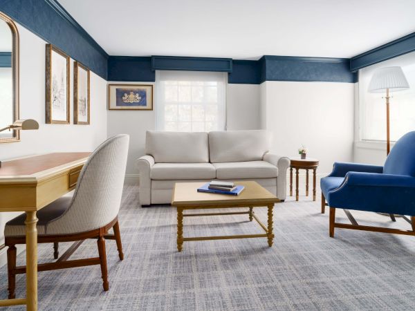 A bright living room with a light gray sofa, blue walls trim, blue armchair, wooden coffee table, desk, framed art, and a floor lamp. End.