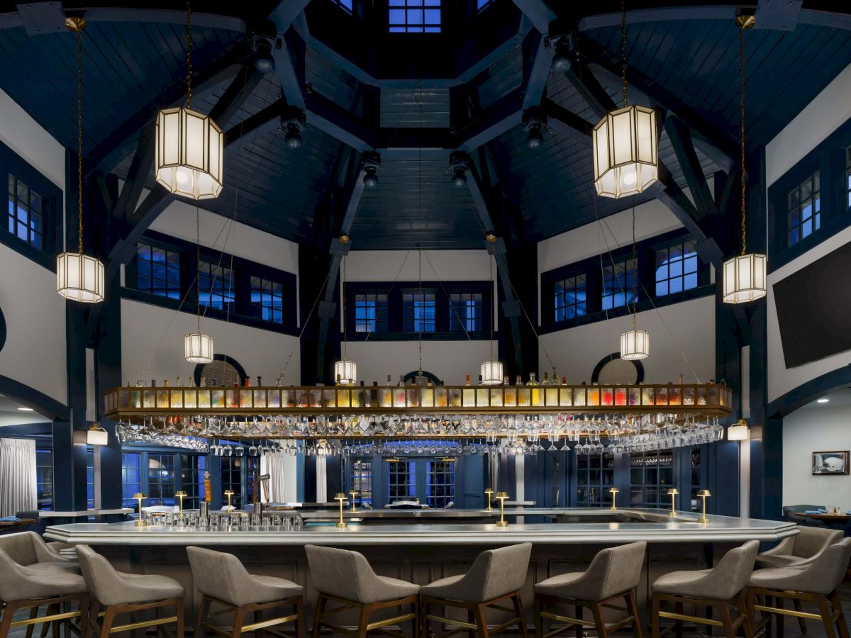 A stylish bar with a long counter, hanging lanterns, high ceiling, and blue accents; chairs line the bar, warm lighting creates a cozy vibe.