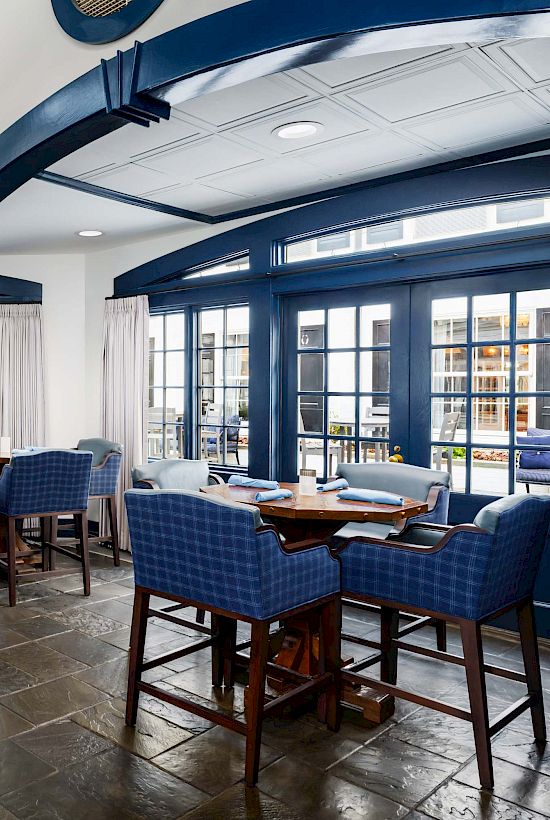 A bright, elegant dining room with blue accents, wooden tables, and wicker chairs in a sunny, airy space.