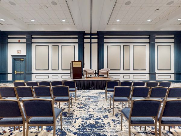 A conference room set up for a presentation or meeting with chairs facing a small table and podium at the front. (140 chars).