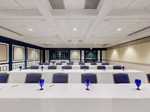 A conference room set up for a formal meeting with long white tables, blue chairs, and blue goblets arranged neatly along the tables.
