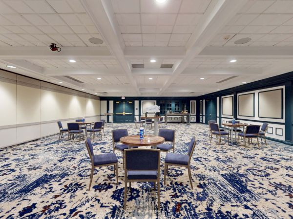 A large, empty conference room with blue and white decor, round tables, chairs, and a patterned carpet, set up for an event in a hotel banquet hall.