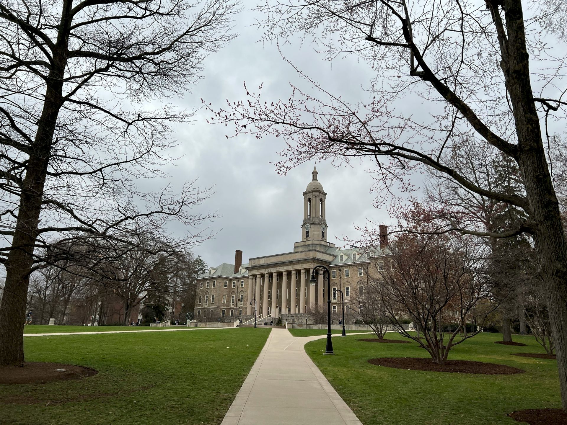 A grand, neoclassical campus building with a central tower, lined by bare trees and a straight path leading to the entrance.