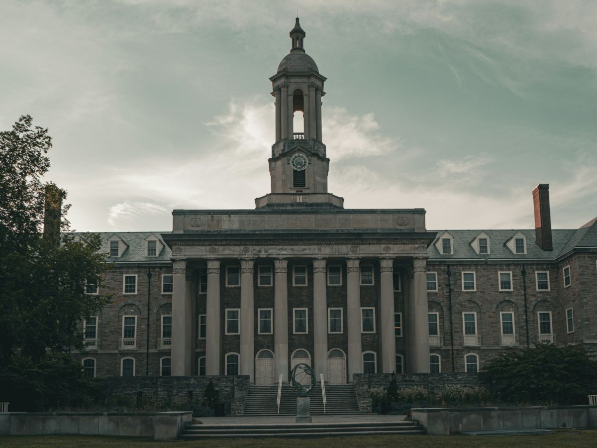 A grand college building with a central tower, columns, and steps leading up, set against a cloudy sky. Top it at 140 characters, always ending the sentence.