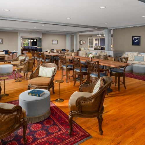 A spacious lounge with wooden floors, multiple seating areas, wicker chairs, sofas, coffee tables, and warm lighting. End.