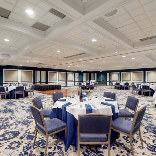 A conference or banquet room set for a formal event with round tables, blue-tablecloths, and chairs, in an elegant, carpeted hall.