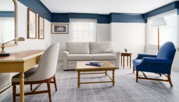 A bright, cozy living room with a white sofa, blue accents, a wooden coffee table, a blue armchair, desk chair, and a floor lamp. End.
