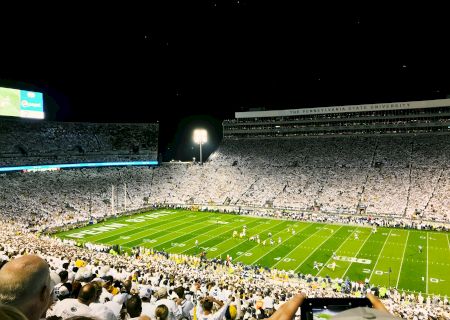 A nighttime stadium scene with a lit field, empty stands, and a few bright screens; looks like a sports event under floodlights.