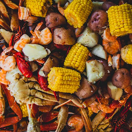 A pile of roasted seafood and veggies&mdash;shrimp, crab legs, corn on the cob, and potatoes&mdash;spread on a grill-ready platter.