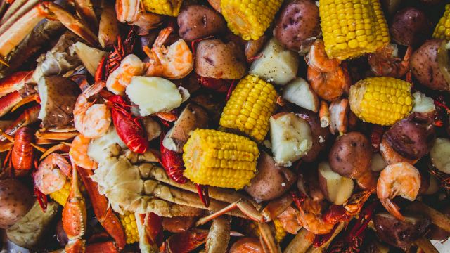 A pile of roasted seafood and veggies&mdash;shrimp, crab legs, corn on the cob, and potatoes&mdash;spread on a grill-ready platter.