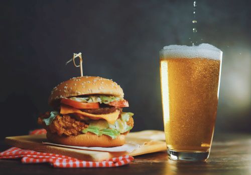 A juicy fried chicken burger with lettuce and tomato beside a frosty glass of beer, on a rustic wooden table.