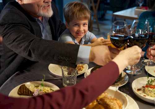 A family cheers with wine glasses at a dinner table, sharing a meal together.