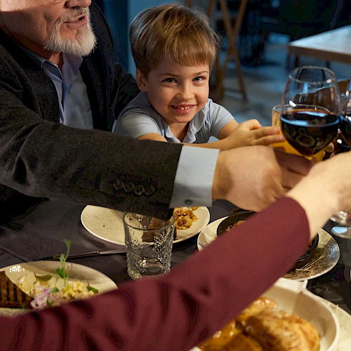 A family cheers with wine glasses at a dinner table, sharing a meal together.