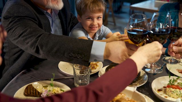 A family cheers with wine glasses at a dinner table, sharing a meal together.