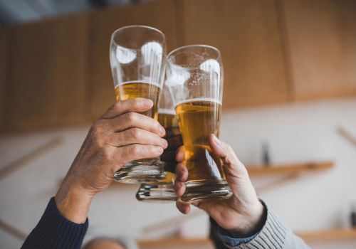 A group of hands clinking three beer glasses in a toast.