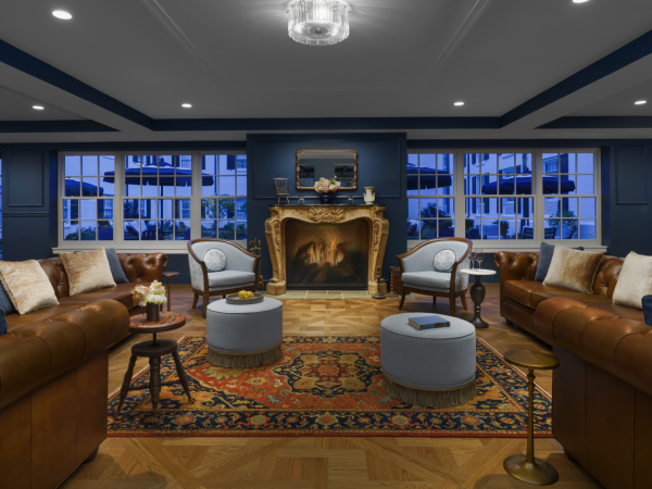 A luxurious living room with brown leather sofas, blue walls, a grand fireplace, ornate golden mirror, and multiple cushioned stools around a patterned rug, chic lighting.