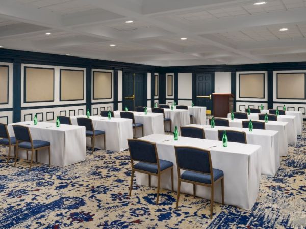 An elegant banquet room with tables covered in white cloth, blue chairs, and green bottles on each table.