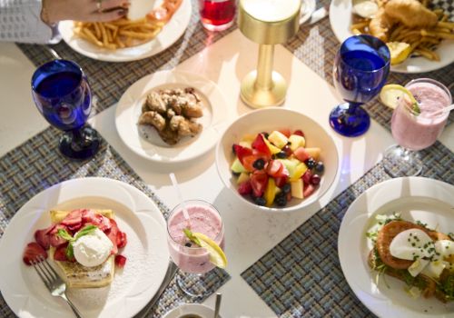 A dining table set with fries, fresh fruit salad, pastries, and pink/blue drinks in glasses, ready to eat.