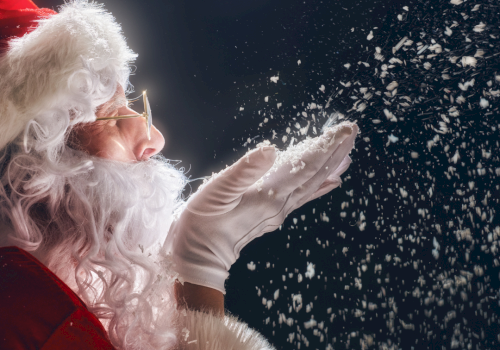 A Santa in red and white tosses glittery flakes/confetti into the night sky.