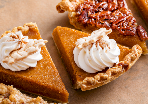 Whipped-cream-topped caramel pecan tart slices on parchment paper.
